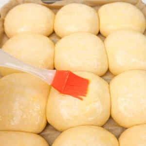 Brushing egg wash on freshly shaped burger buns before baking.