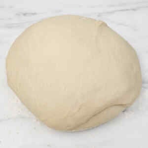 A round ball of dough on a marble surface, ready for making burger buns.