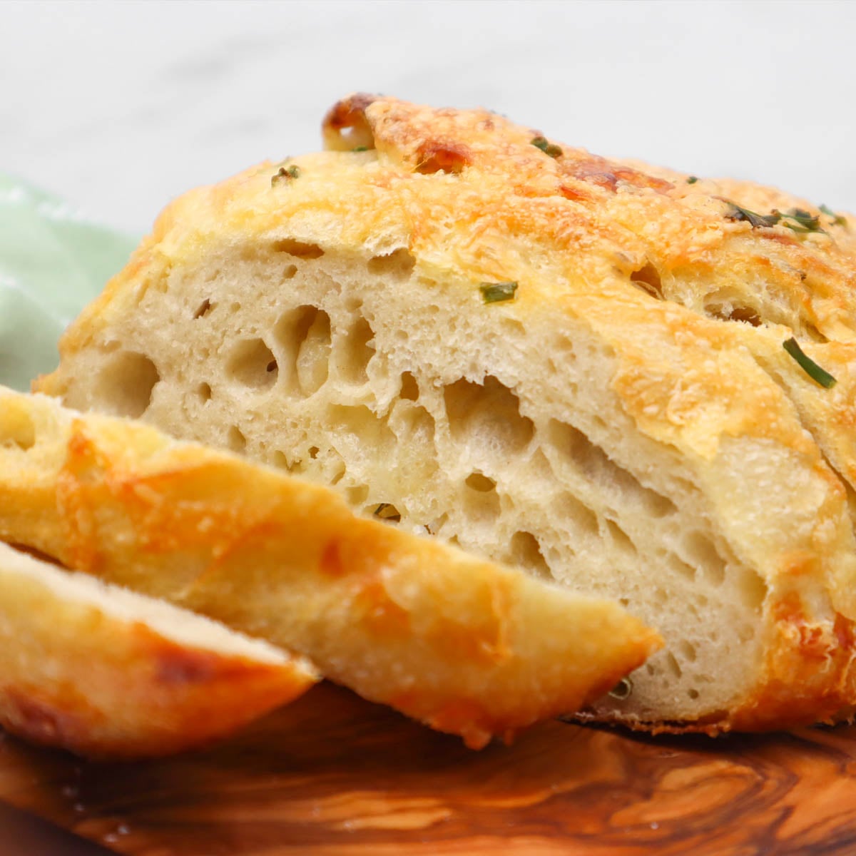 Cheese and Chive Sourdough Loaf Close-up of a sliced rustic cheese and chive sourdough loaf, showcasing its airy texture and golden crust.