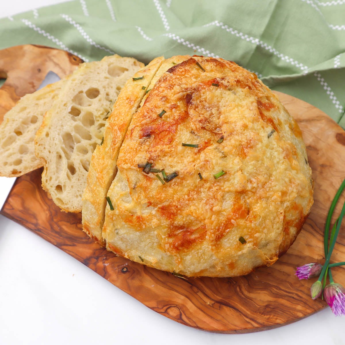Cheese and Chive Sourdough Loaf A rustic cheese and chive sourdough loaf with slices on a wooden board.