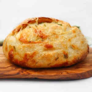 A golden-brown cheese and chive sourdough loaf resting on a wooden board.