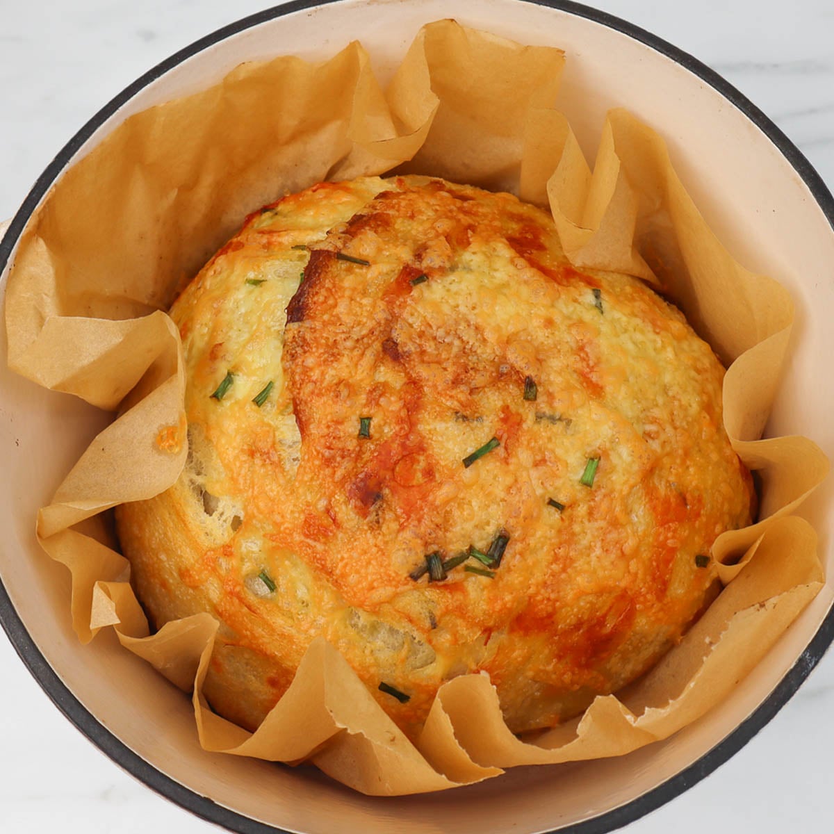 Cheese and Chive Sourdough Loaf A freshly baked cheese and chive sourdough loaf resting in a pot lined with parchment paper.