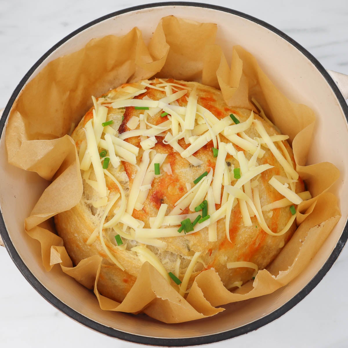 Cheese and Chive Sourdough Loaf A rustic cheese and chive sourdough loaf topped with shredded cheese and chives, resting in a baking pot.