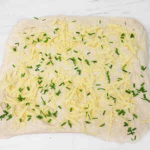Sourdough dough topped with shredded cheese and chopped chives, ready for baking.