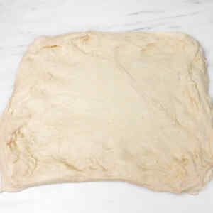 A square piece of sourdough bread dough on a marble surface.