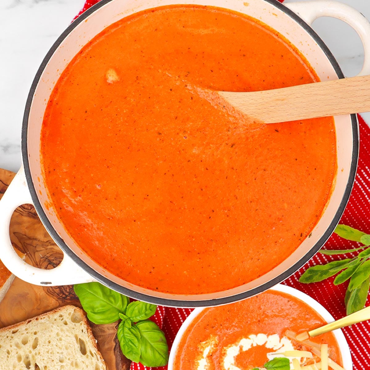 Cheesy Roasted Red Pepper Soup A creamy, vibrant red pepper soup in a pot, garnished with basil and served with bread.