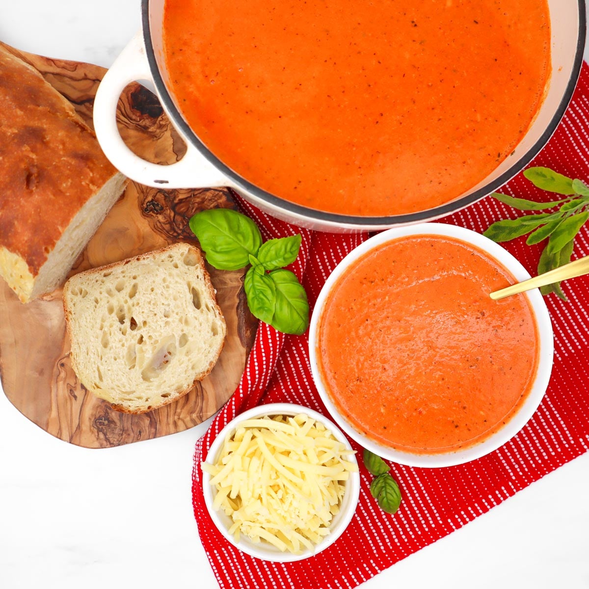 Cheesy Roasted Red Pepper Soup A bowl of cheesy roasted red pepper soup with a spoon, accompanied by bread and cheese on a wooden board.