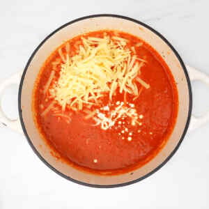 Cheesy roasted red pepper soup with shredded cheese on top in a pot.