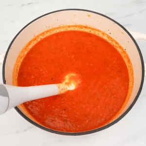 A creamy, vibrant red pepper soup being blended in a pot.