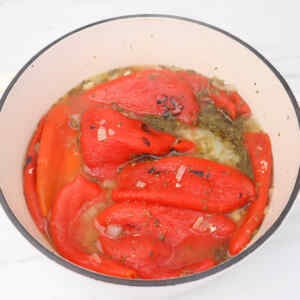 A pot filled with roasted red peppers and herbs in broth.