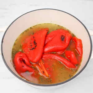 A pot filled with roasted red peppers in broth, garnished with herbs.