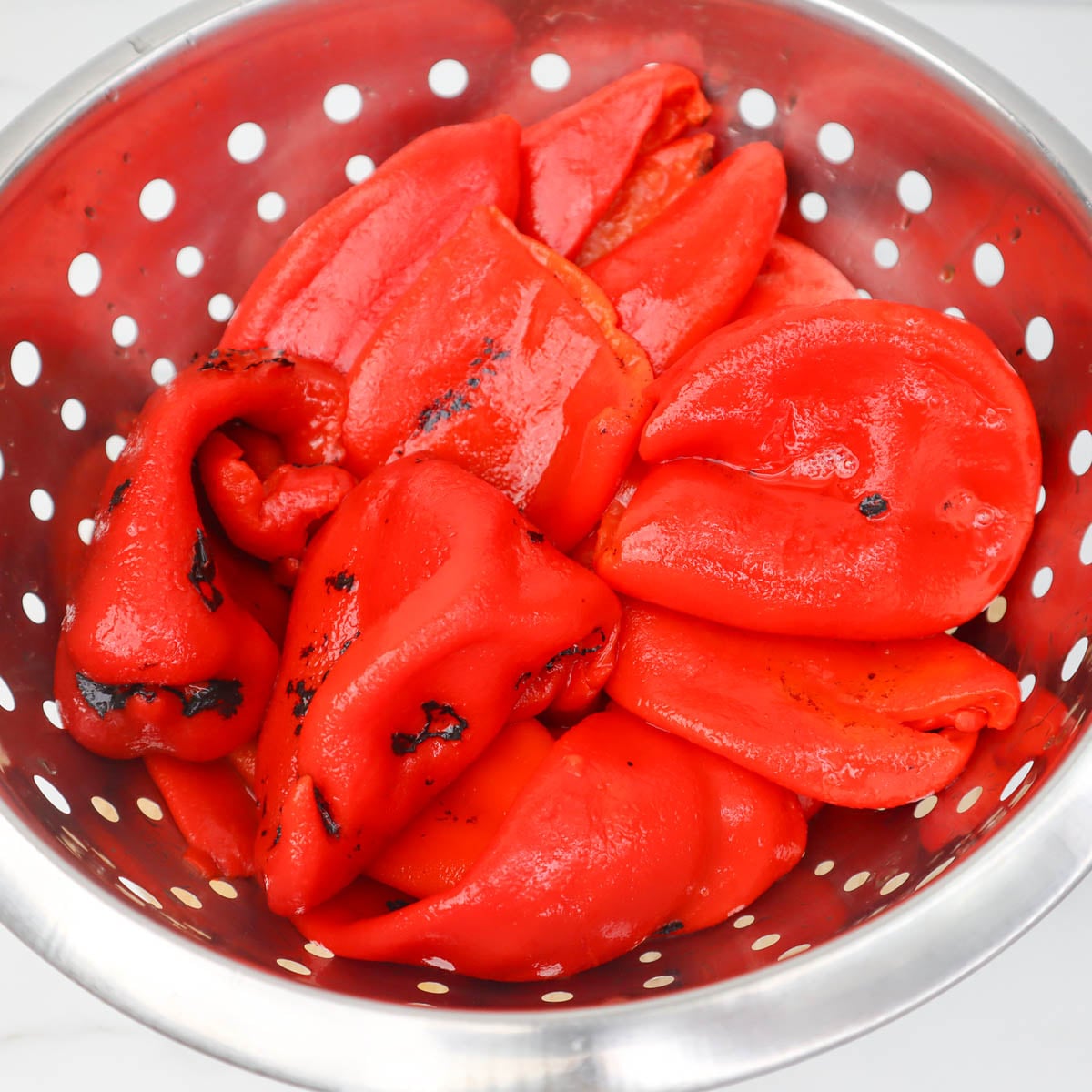 Cheesy Roasted Red Pepper Soup Roasted red peppers in a colander, ready to be used in a cheesy soup.