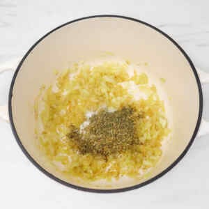 Chopped onions and herbs sautéing in a pot for soup preparation.