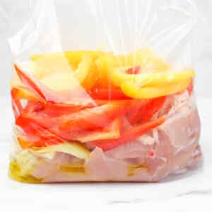 Chicken and sliced bell peppers in a freezer bag for meal prep.