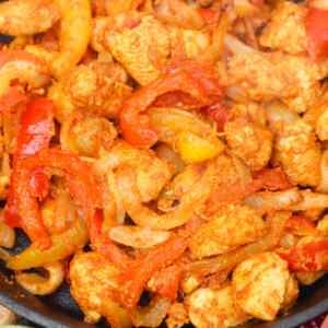 Sautéed chicken with colorful bell peppers and onions in a skillet.