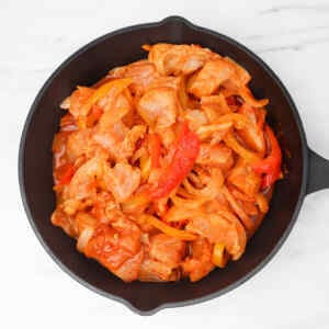 Cooked chicken fajitas with bell peppers and onions in a skillet.