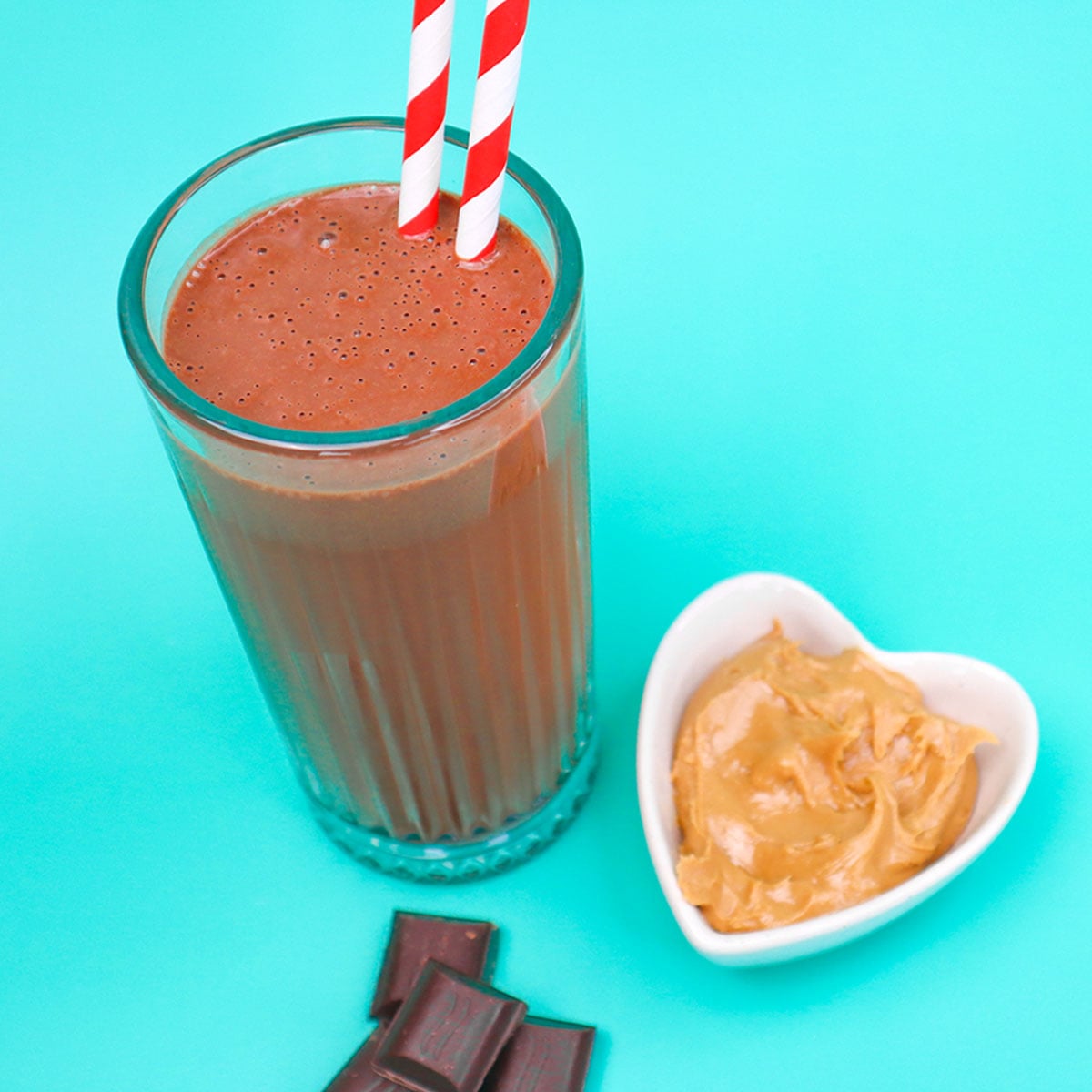 Chocolate Peanut Butter Smoothie Freezer Meal Prep Packs A glass of chocolate peanut butter smoothie with red and white striped straws next to a bowl of peanut butter.