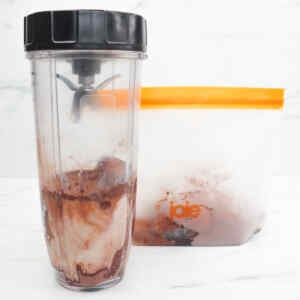A blender filled with a chocolate peanut butter smoothie next to a freezer meal prep container.