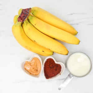 Ingredients for a chocolate peanut butter smoothie, including bananas, peanut butter, cocoa powder, and milk.
