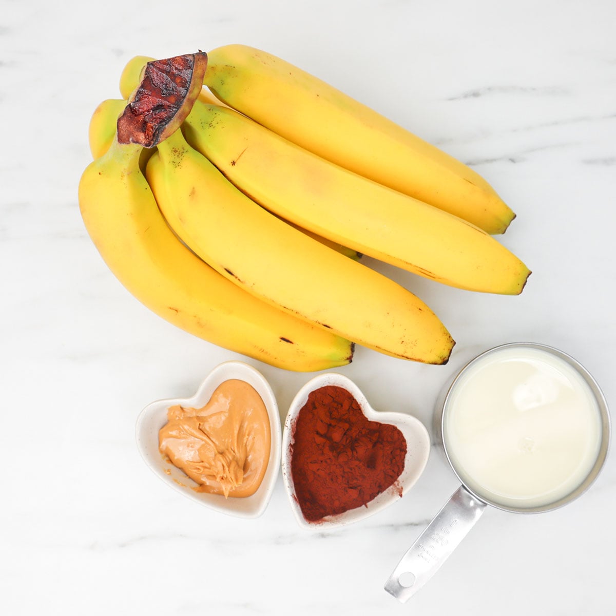 Chocolate Peanut Butter Smoothie Freezer Meal Prep Packs Ingredients for a chocolate peanut butter smoothie, including bananas, peanut butter, cocoa powder, and milk.