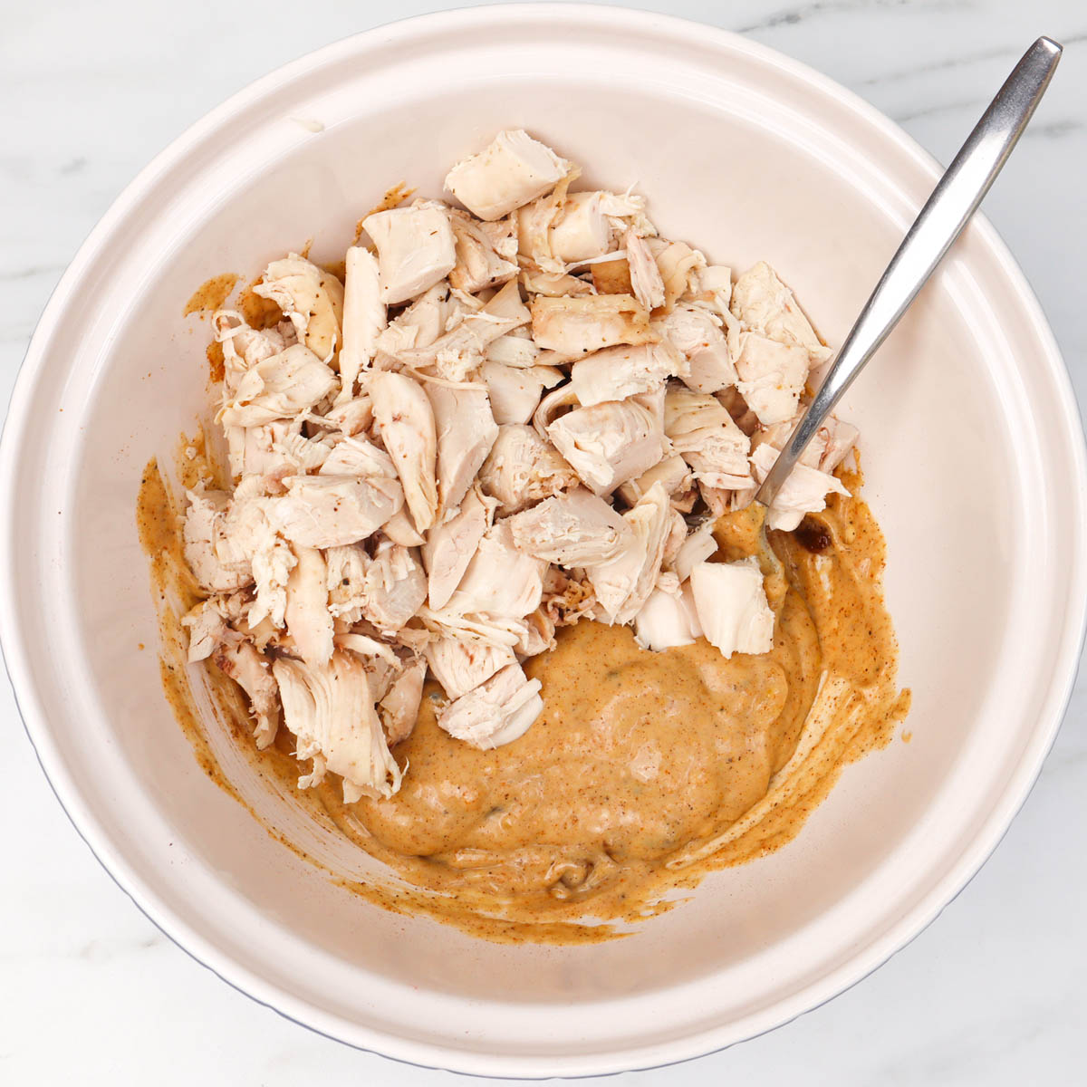 Coronation Chicken Chopped cooked chicken mixed with a creamy sauce in a bowl.