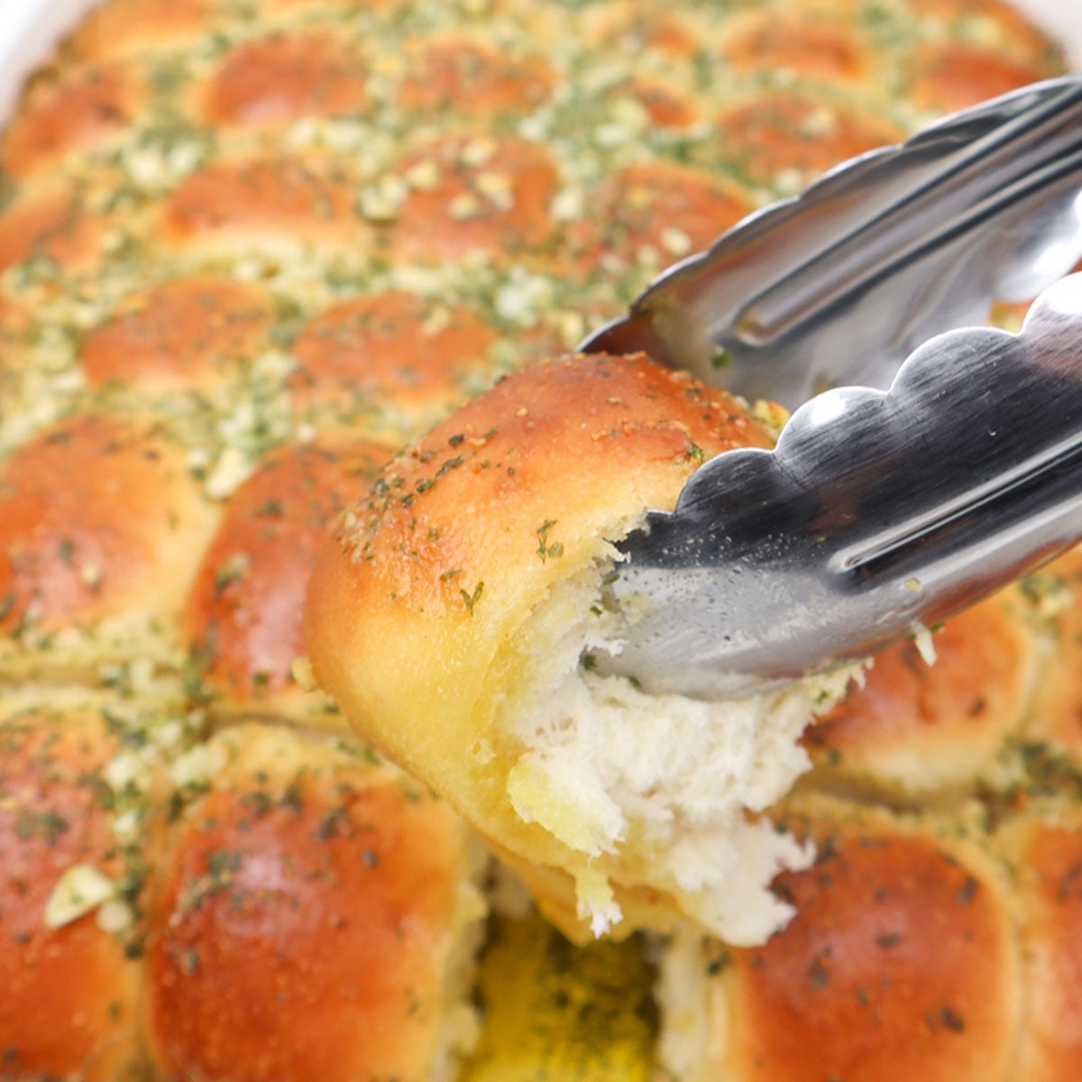 Garlic Dough Balls A garlic dough ball being lifted with tongs, showcasing its fluffy interior and golden crust.