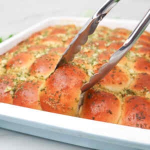 Garlic dough balls being served with tongs from a baking dish.