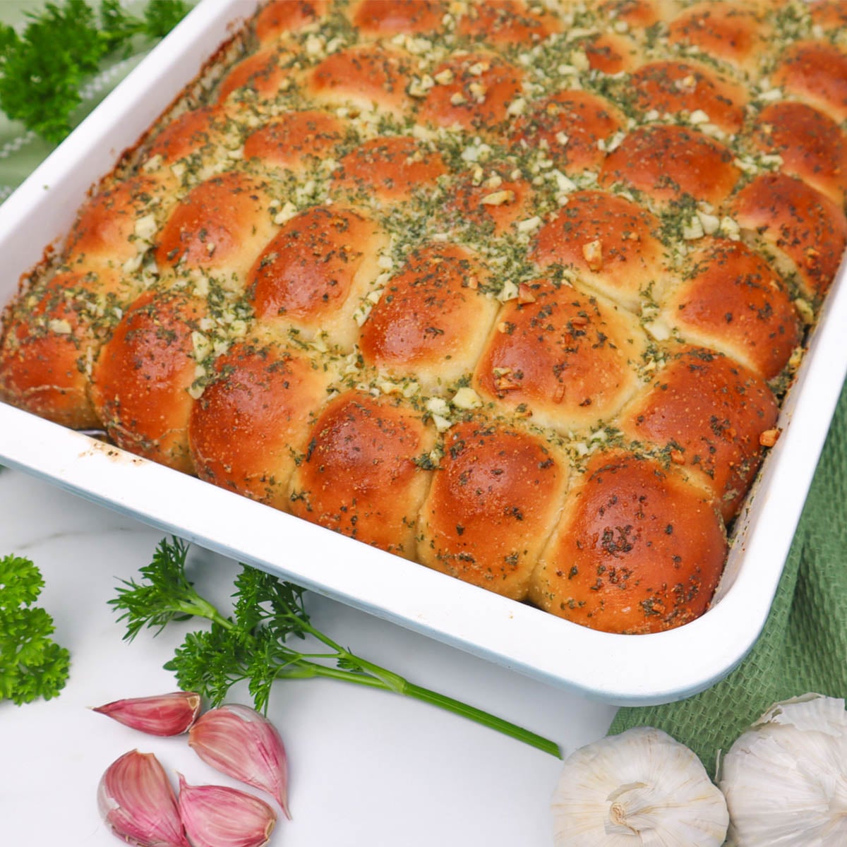 Garlic Dough Balls Golden garlic dough balls topped with herbs in a baking dish, surrounded by garlic cloves and parsley.
