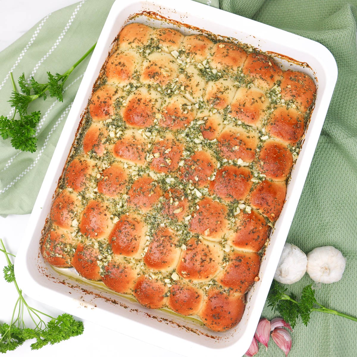 Garlic Dough Balls Golden garlic dough balls topped with herbs in a white baking dish, surrounded by fresh garlic and parsley.