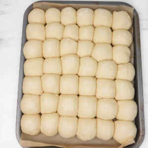A tray filled with neatly arranged, uncooked garlic dough balls ready for baking.