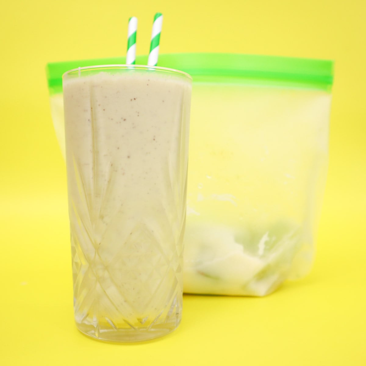 Kiwi and Avocado Smoothie Freezer Meal Prep Packs A glass of kiwi and avocado smoothie with green straws next to a freezer bag.