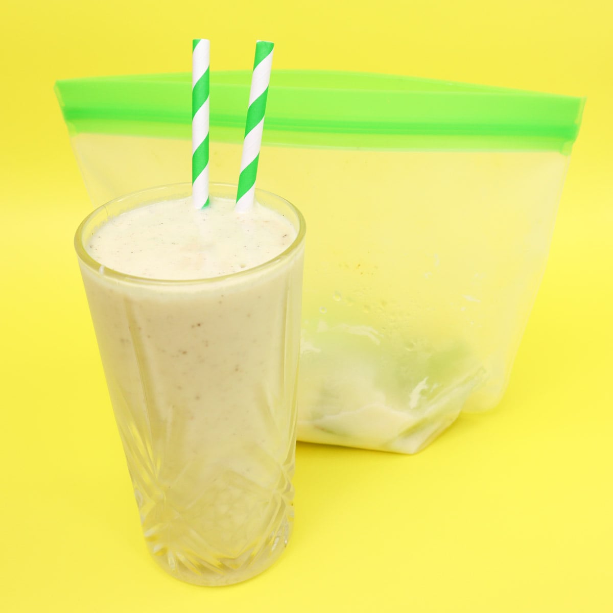 Kiwi and Avocado Smoothie Freezer Meal Prep Packs A glass of kiwi and avocado smoothie with green straws next to a freezer bag.