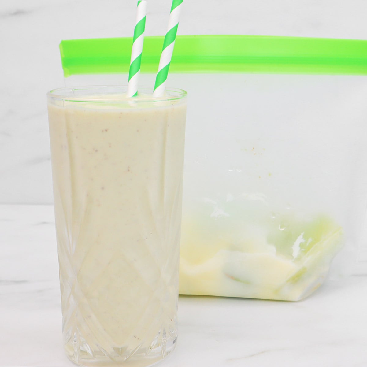 Kiwi and Avocado Smoothie Freezer Meal Prep Packs A glass of kiwi and avocado smoothie with green striped straws next to a freezer bag.