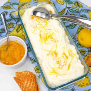 A dish of creamy lemon ice cream topped with lemon zest, next to a bowl of lemon sauce and waffle cones.