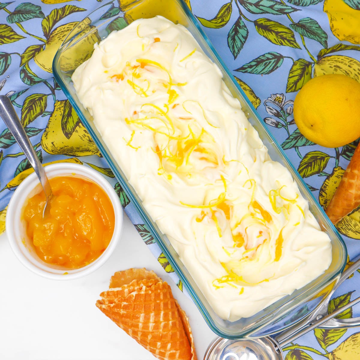 Lemon Ice Cream A dish of creamy lemon ice cream topped with lemon zest, alongside lemon curd and waffle cones.