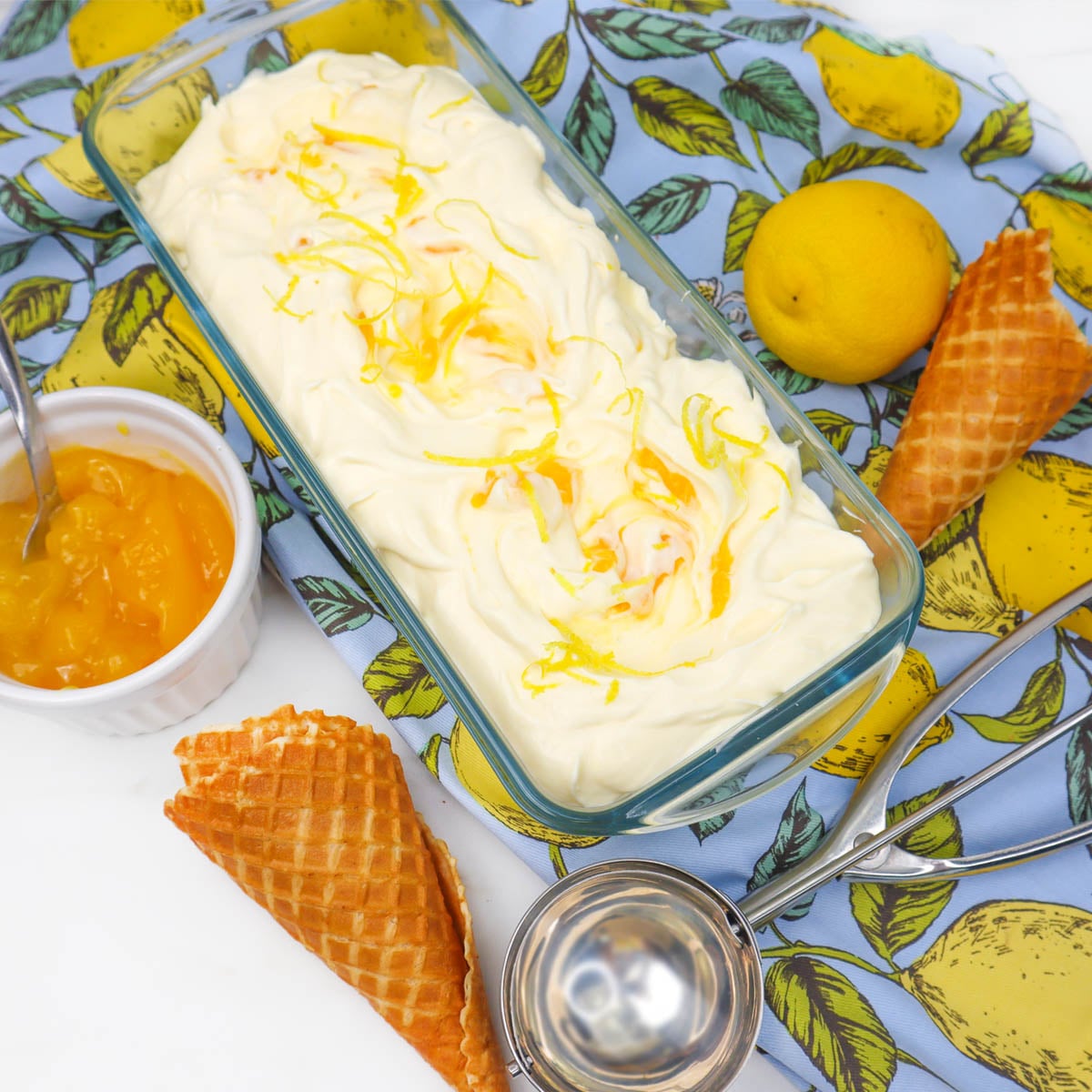 Lemon Ice Cream A bowl of creamy lemon ice cream topped with lemon zest, surrounded by a lemon, waffle cones, and lemon curd.