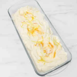 A creamy lemon ice cream topped with lemon zest in a glass dish.