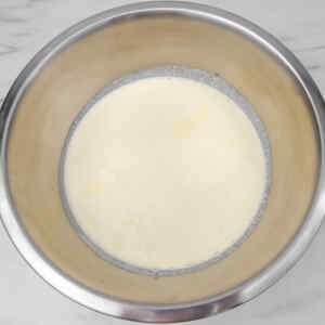 A stainless steel bowl filled with a creamy lemon ice cream mixture.