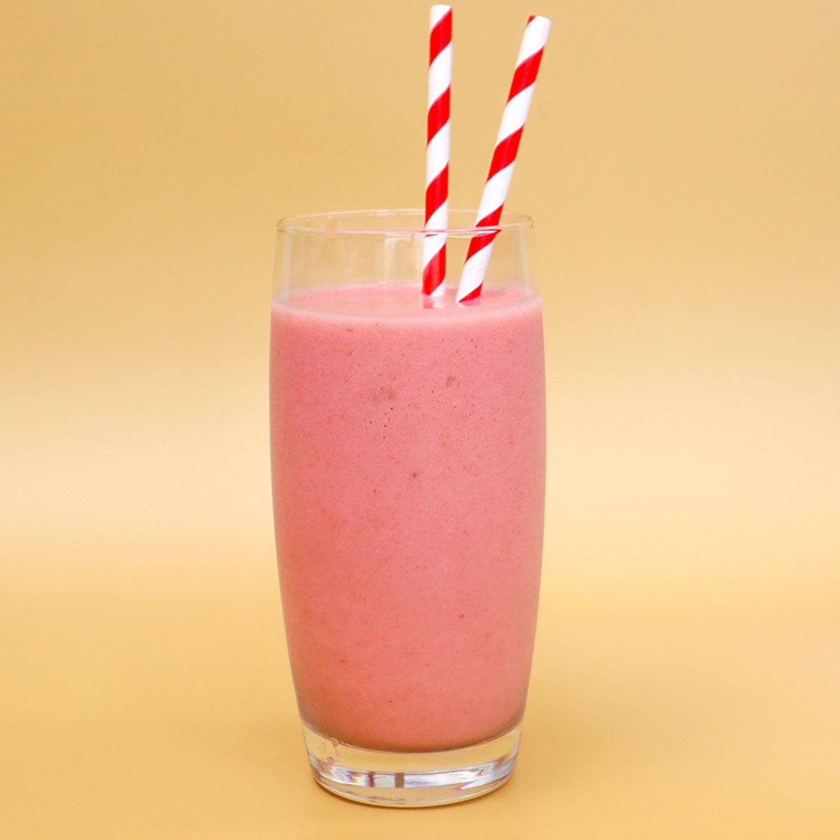 Raspberry Banana Smoothie Freezer Meal Prep Packs A pink raspberry banana smoothie in a tall glass with two red and white striped straws.