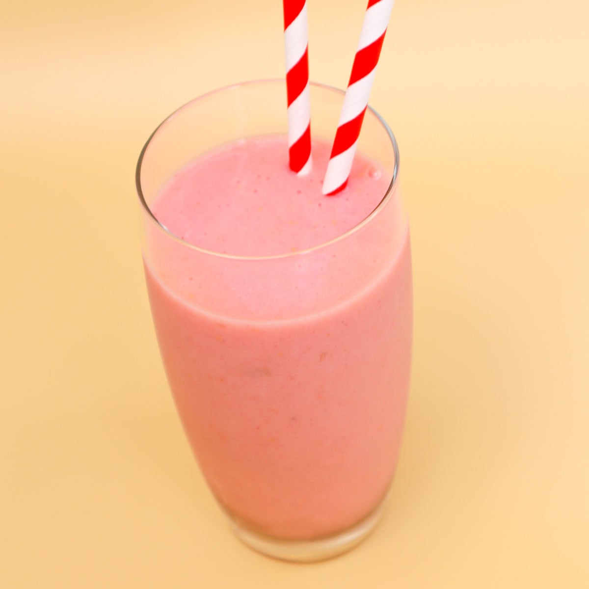 Raspberry Banana Smoothie Freezer Meal Prep Packs A glass of raspberry banana smoothie with red and white striped straws.
