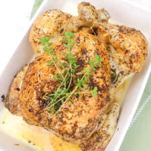 A perfectly roasted chicken garnished with fresh herbs in a baking dish.