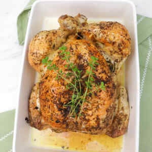 A perfectly roasted chicken garnished with fresh herbs in a white dish.