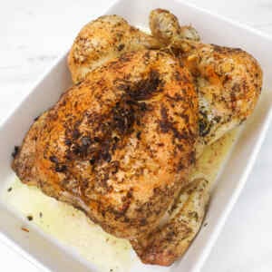A perfectly roasted chicken seasoned with herbs, resting in a white dish.