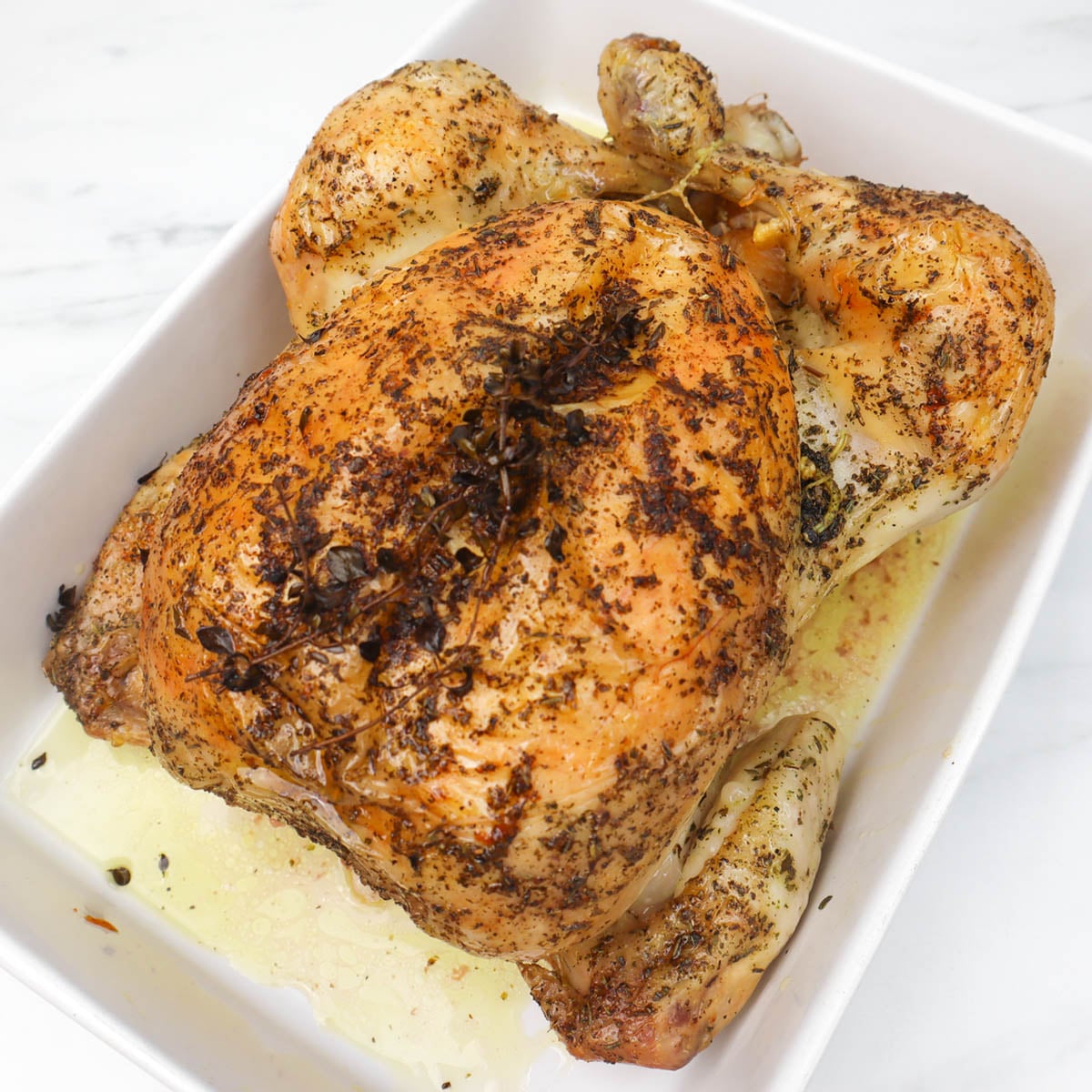 Roast Chicken A perfectly roasted chicken seasoned with herbs, resting in a white dish.