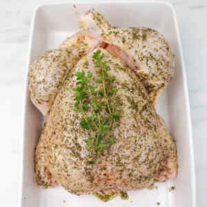 A whole chicken seasoned with herbs, ready for roasting.