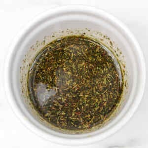 A bowl containing a mixture of herbs and spices in oil.