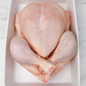 Raw whole chicken prepared for roasting in a white dish.