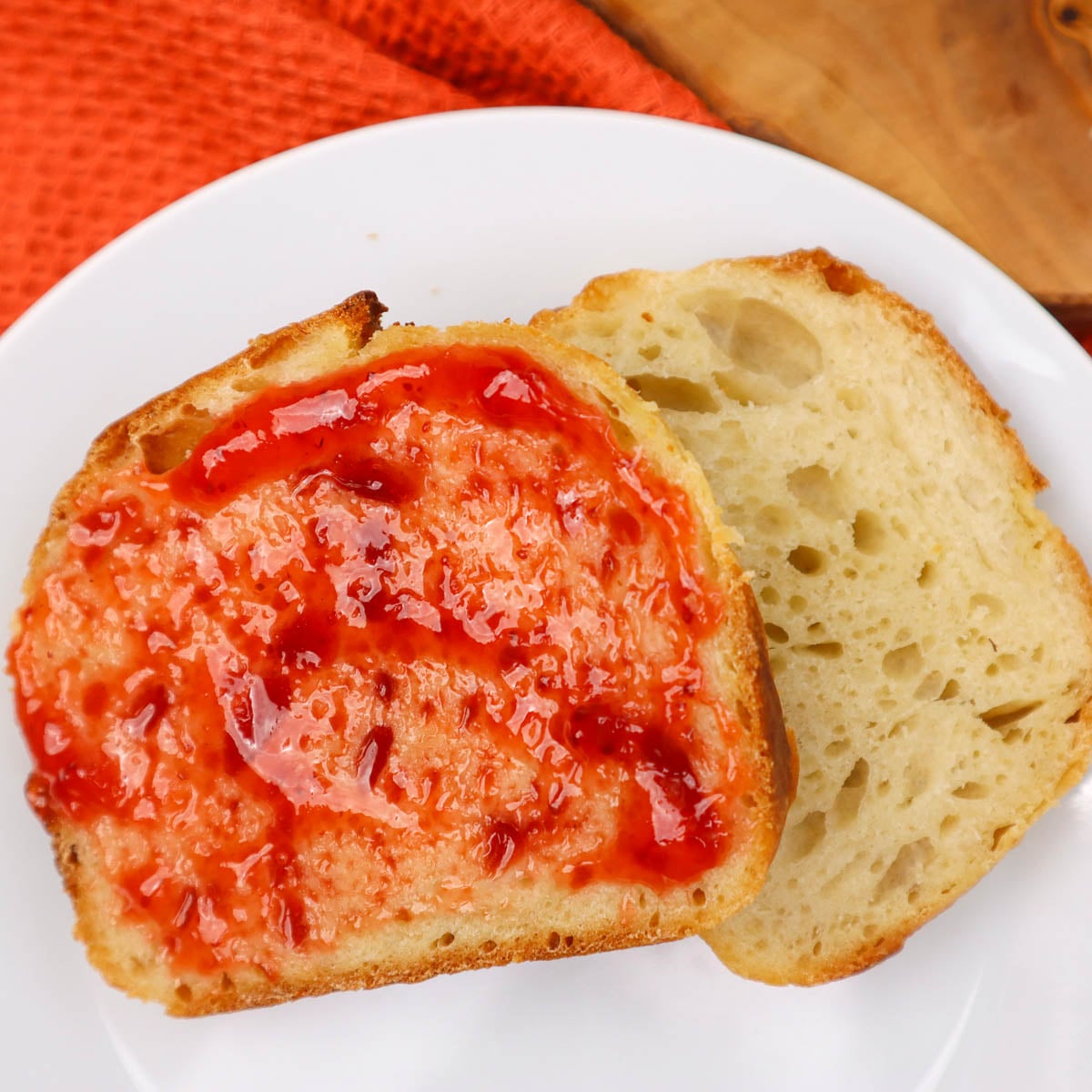 Sourdough Sandwich Loaf A slice of sourdough sandwich loaf topped with strawberry jam, next to a plain slice on a white plate.