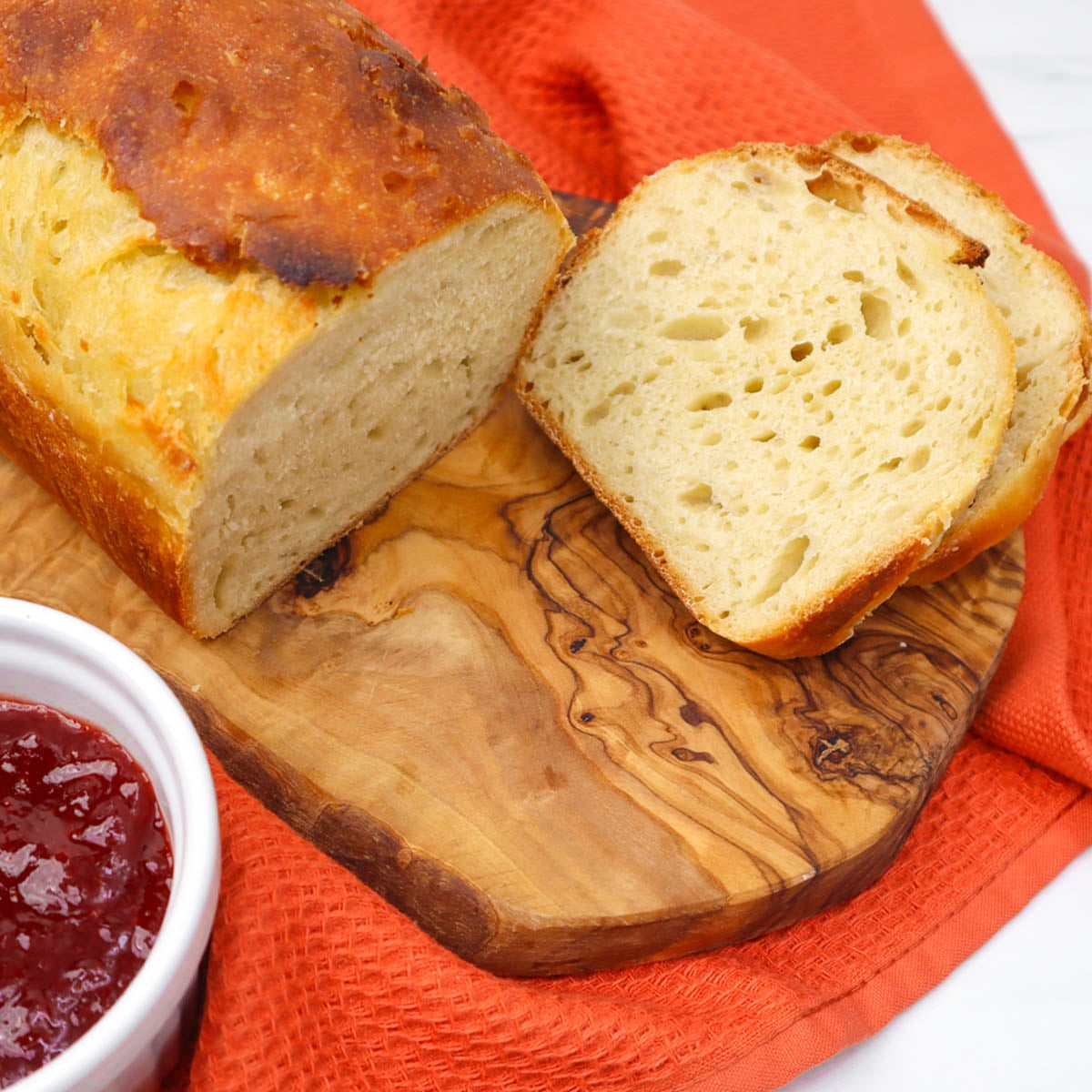 Sourdough Sandwich Loaf Freshly baked sourdough sandwich loaf sliced on a wooden board with a side of jam.