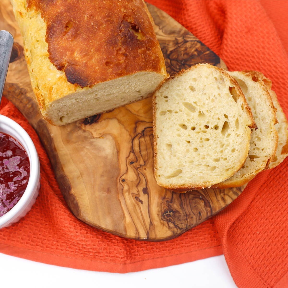 Sourdough Sandwich Loaf Freshly baked sourdough sandwich loaf sliced on a wooden board with a bowl of jam.